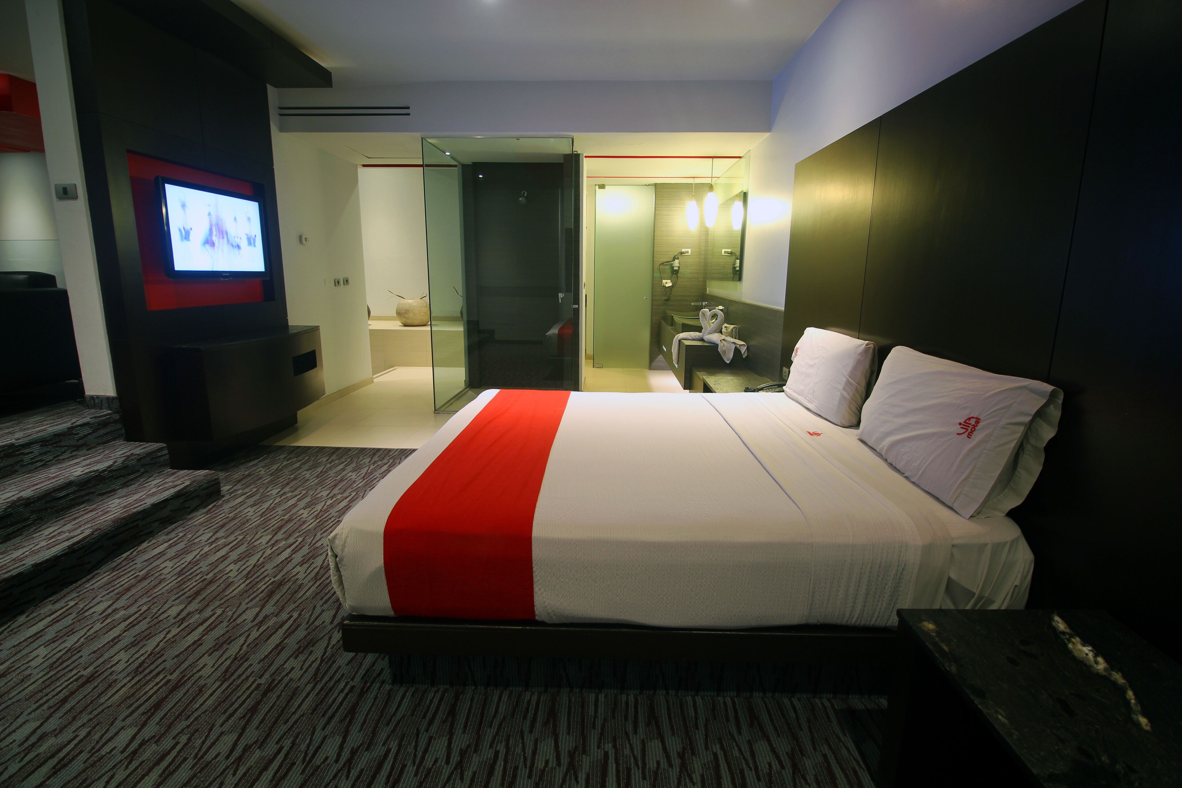 Una habitación de hotel con una cama grande, televisor, baño con espejo y una escalera.
