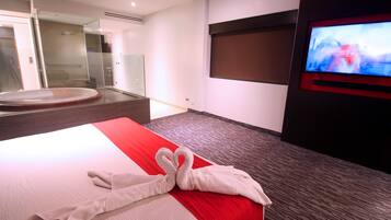 A hotel room with a large bed, a TV on the wall, and a glass-enclosed shower area.