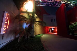 Un edificio con un letrero de neón, palmeras y una entrada iluminada en rojo.