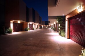Un edificio moderno y bien iluminado, con una puerta de garaje roja, un camino de hormigón y plantas en macetas a lo largo de los laterales.