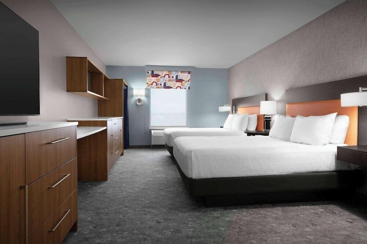 A hotel room with a large bed, a desk, a TV, and a window with a view.