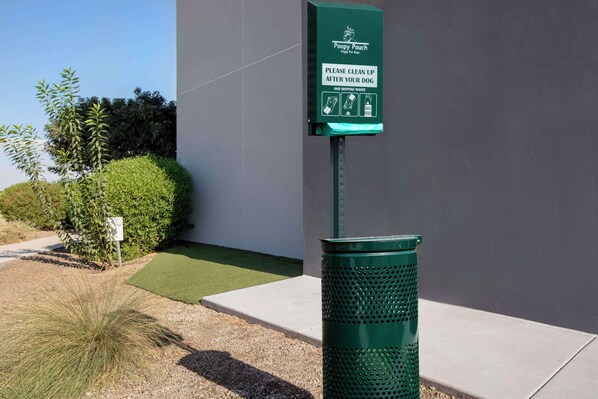 Un bote verde para desechos y un cartel con indicaciones para limpiar después de los perros.