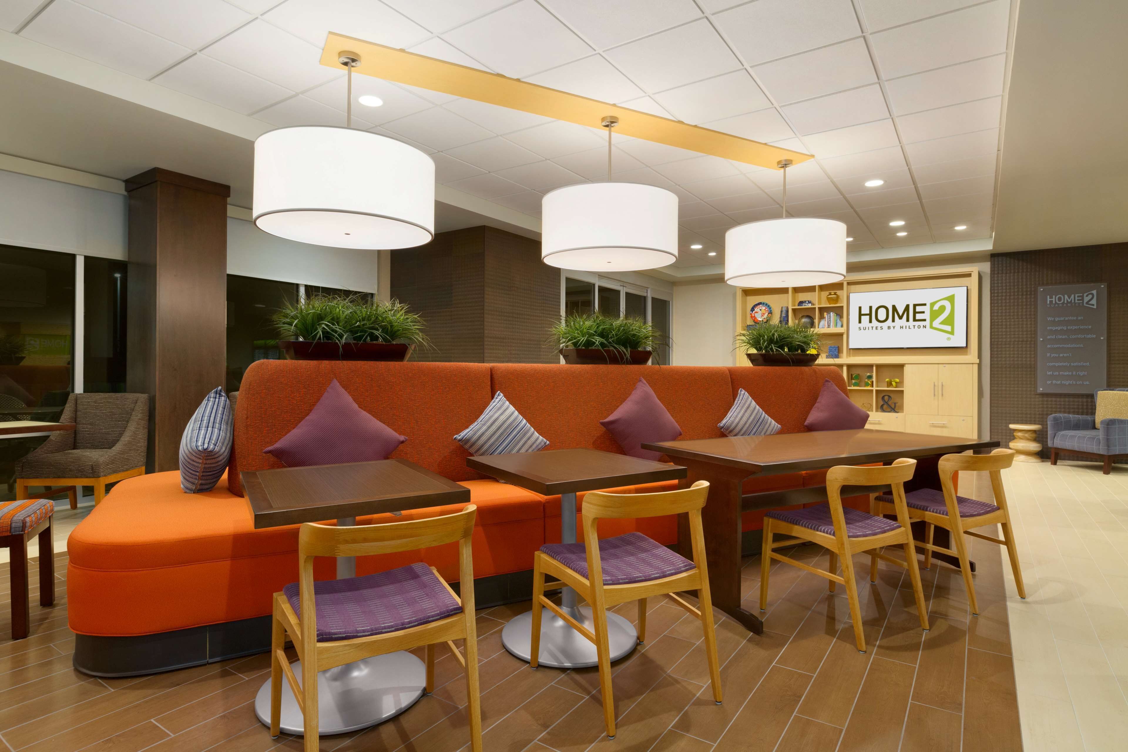 En moderne hotellobby med orange siddemøbler, træborde og hængende lamper.
