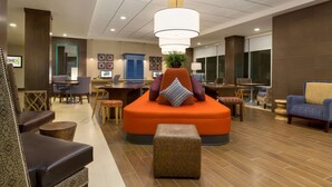 Um lobby moderno com área de estar central em laranja, várias mesas e um grande candelabro.