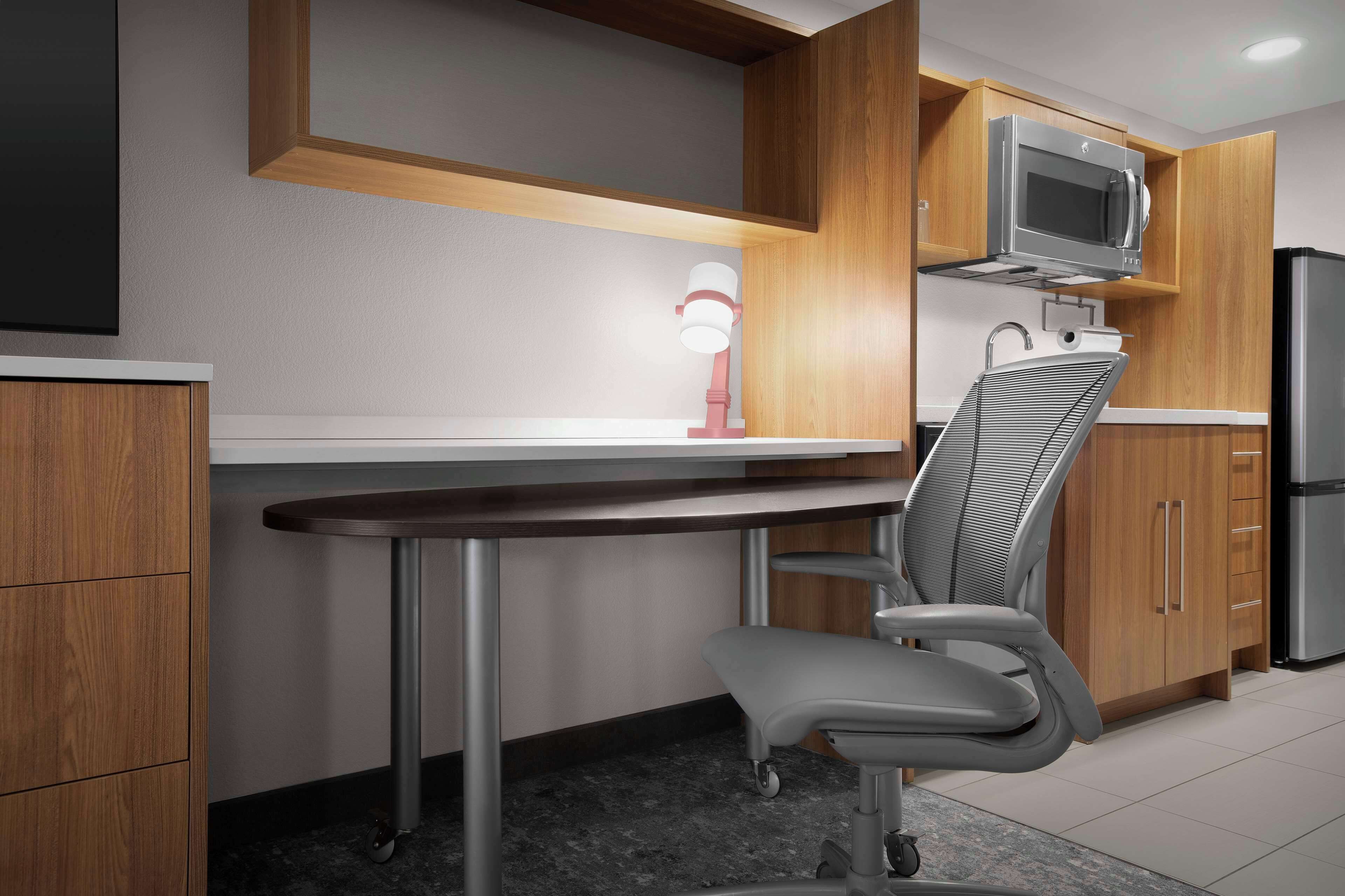 Una cocina moderna con armarios de madera, un refrigerador de acero inoxidable, un microondas y una silla.