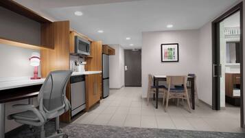 A modern kitchen with a microwave, refrigerator, and wooden cabinets. There is a dining area with a table and chairs.