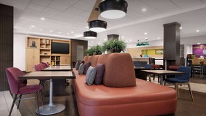 Espaço lounge moderno com uma mesa comprida, assentos acolchoados e iluminação pendente.