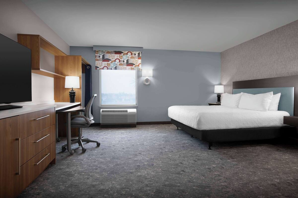 A hotel room with a bed, desk, and TV.