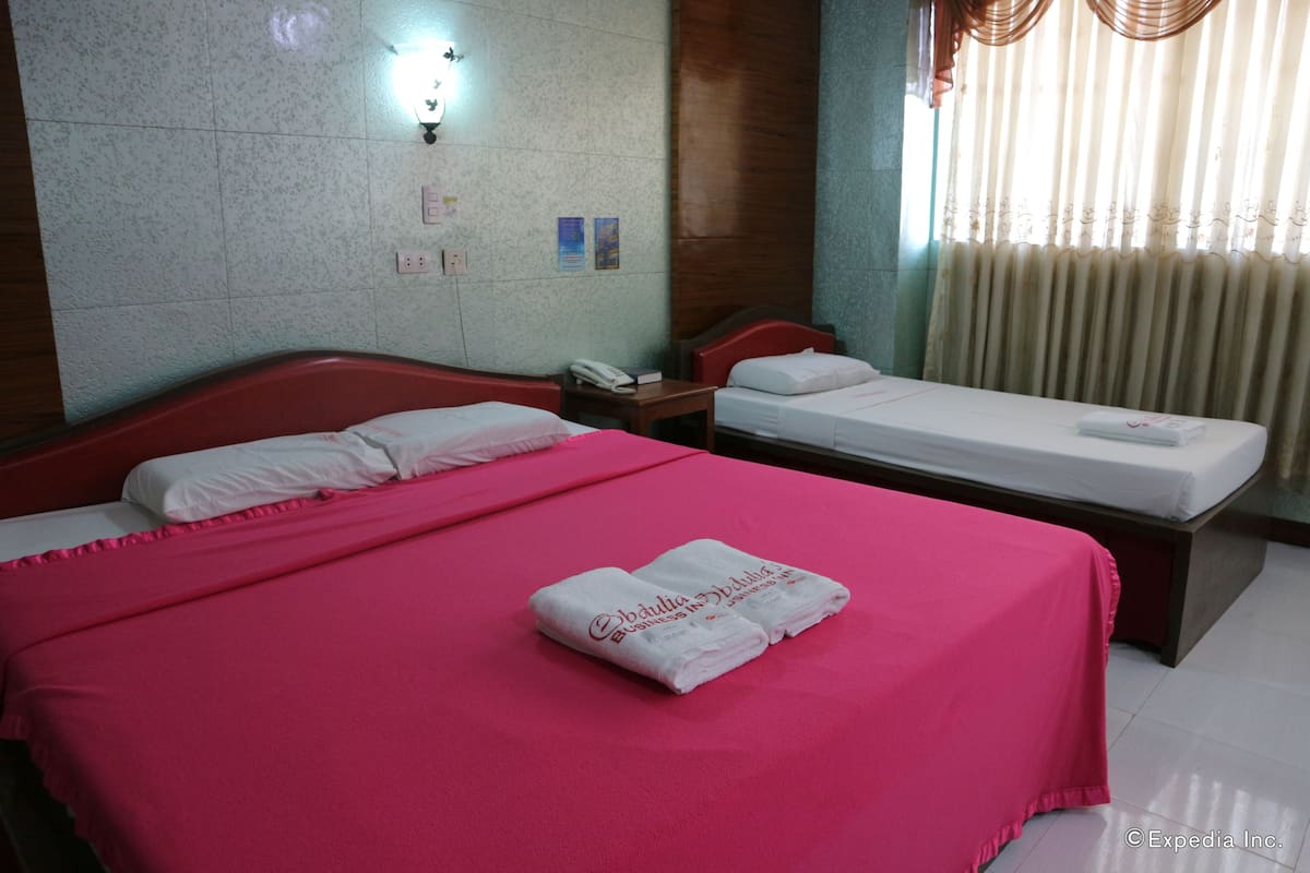 A hotel room with two beds, a wooden headboard, a nightstand, and a wall-mounted light fixture.