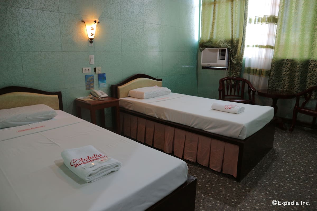 A hotel room with two beds, a bedside telephone, a wall-mounted air conditioner, and a small table with a chair.
