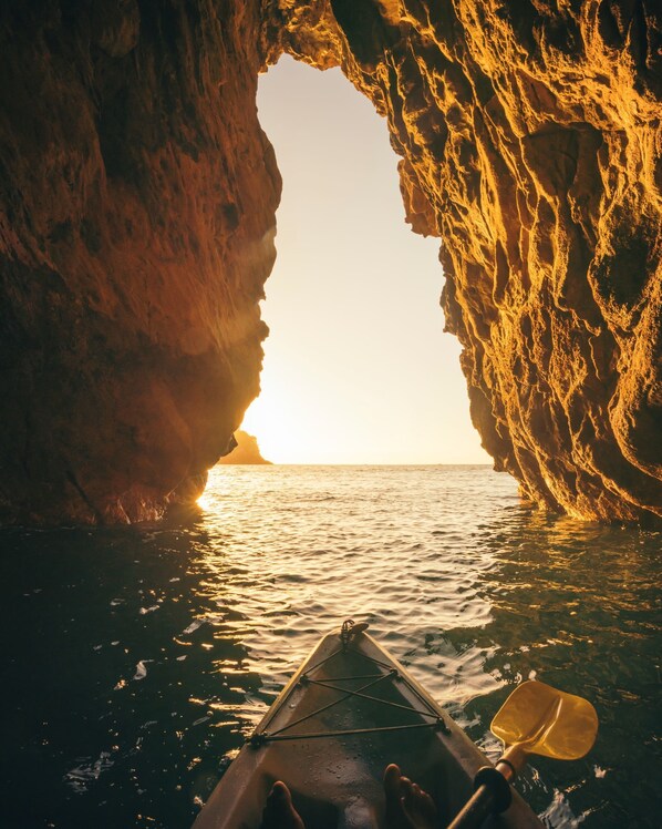 A kayak navigating through a natural rock formation with a view of the sunset over the water.