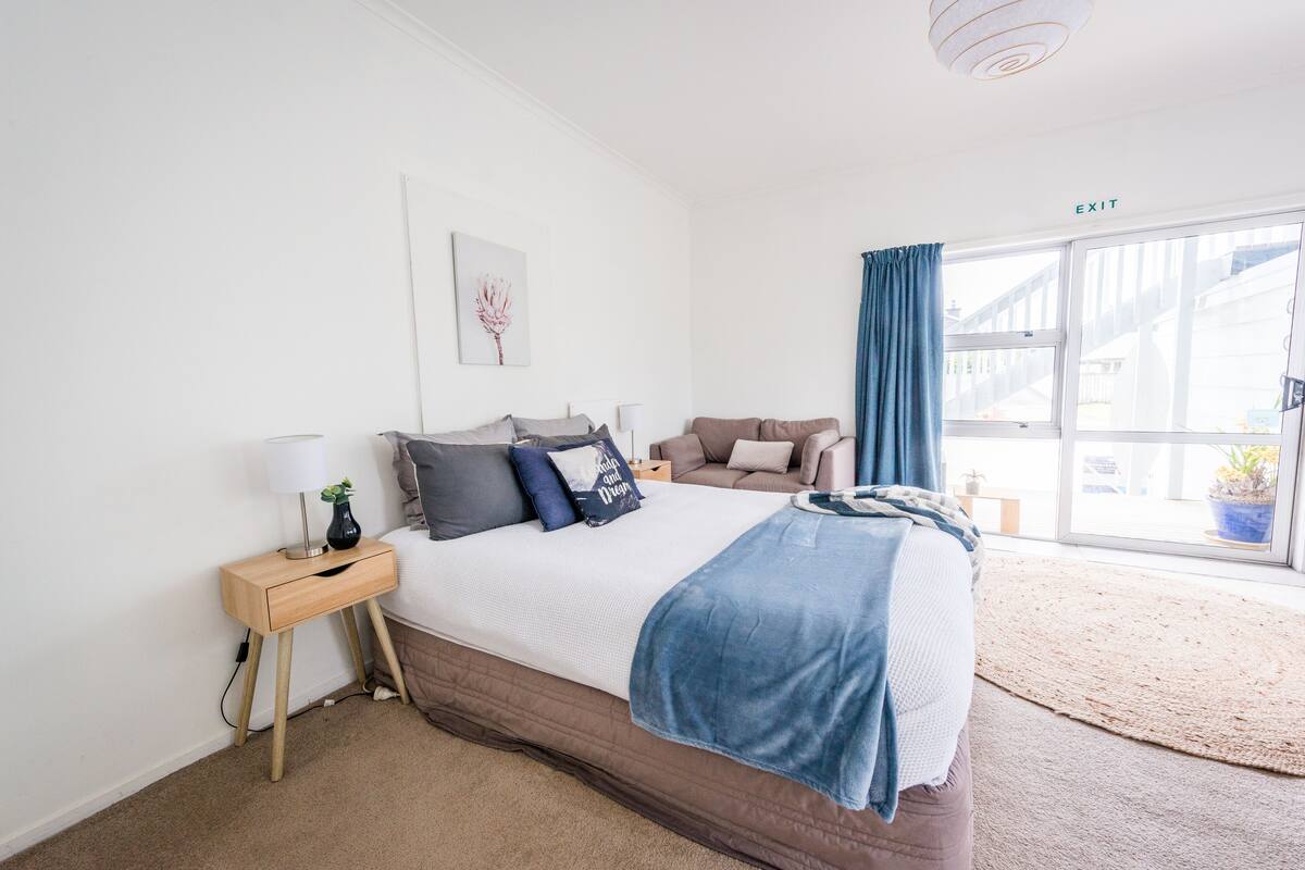 A bedroom with a large bed, a nightstand, a window with curtains, and a view of the outside.