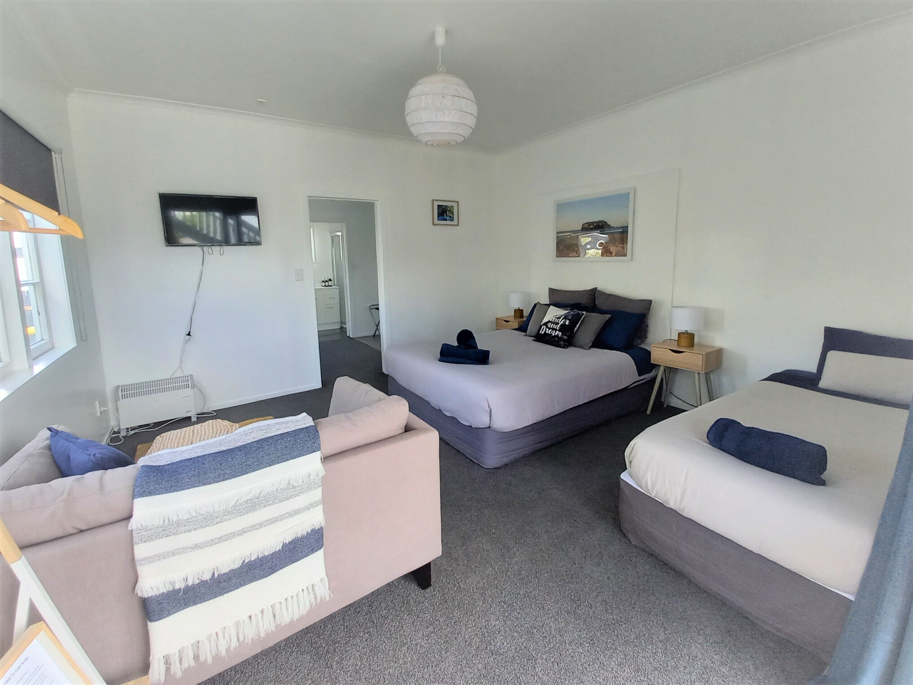 A hotel room with two beds, a sofa, a TV, and a ceiling light.