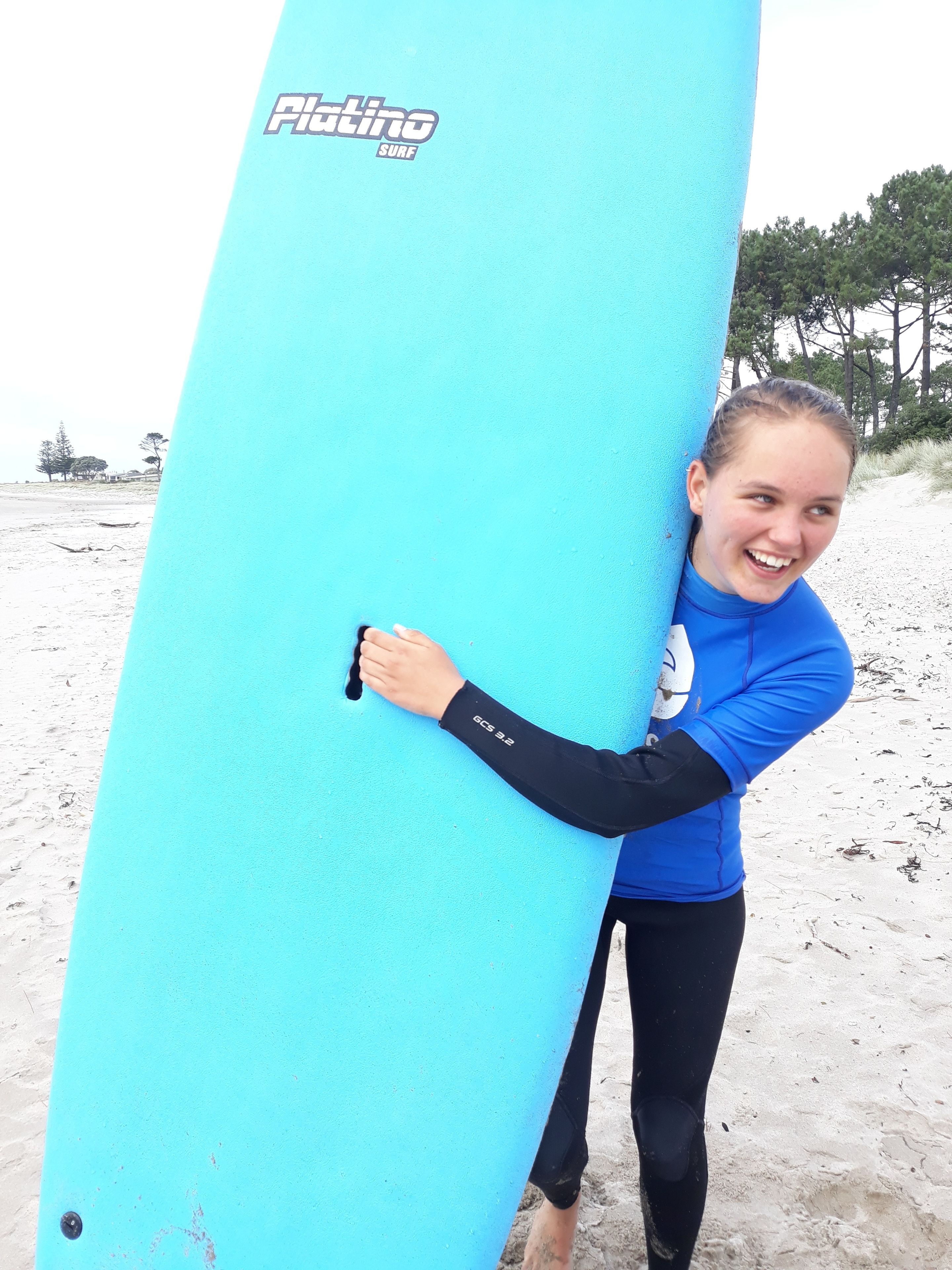 Uma pessoa segurando uma prancha de surf azul com a inscrição 'Piatto Surf'.