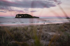 A beach with a person walking, grassy dunes, and a distant island.