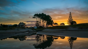 Une scène paisible au bord d’un lac, avec une maison, des arbres et un reflet clair sur l’eau.