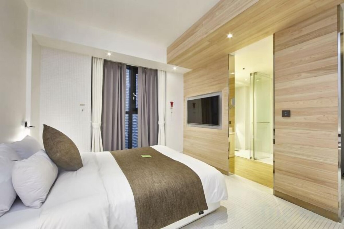 A hotel room with a bed, a TV, a shower, and a wooden wall.