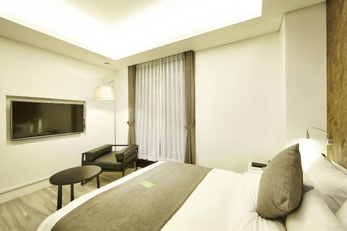 A hotel room with a bed, a desk, a chair, a TV, and a window with curtains.