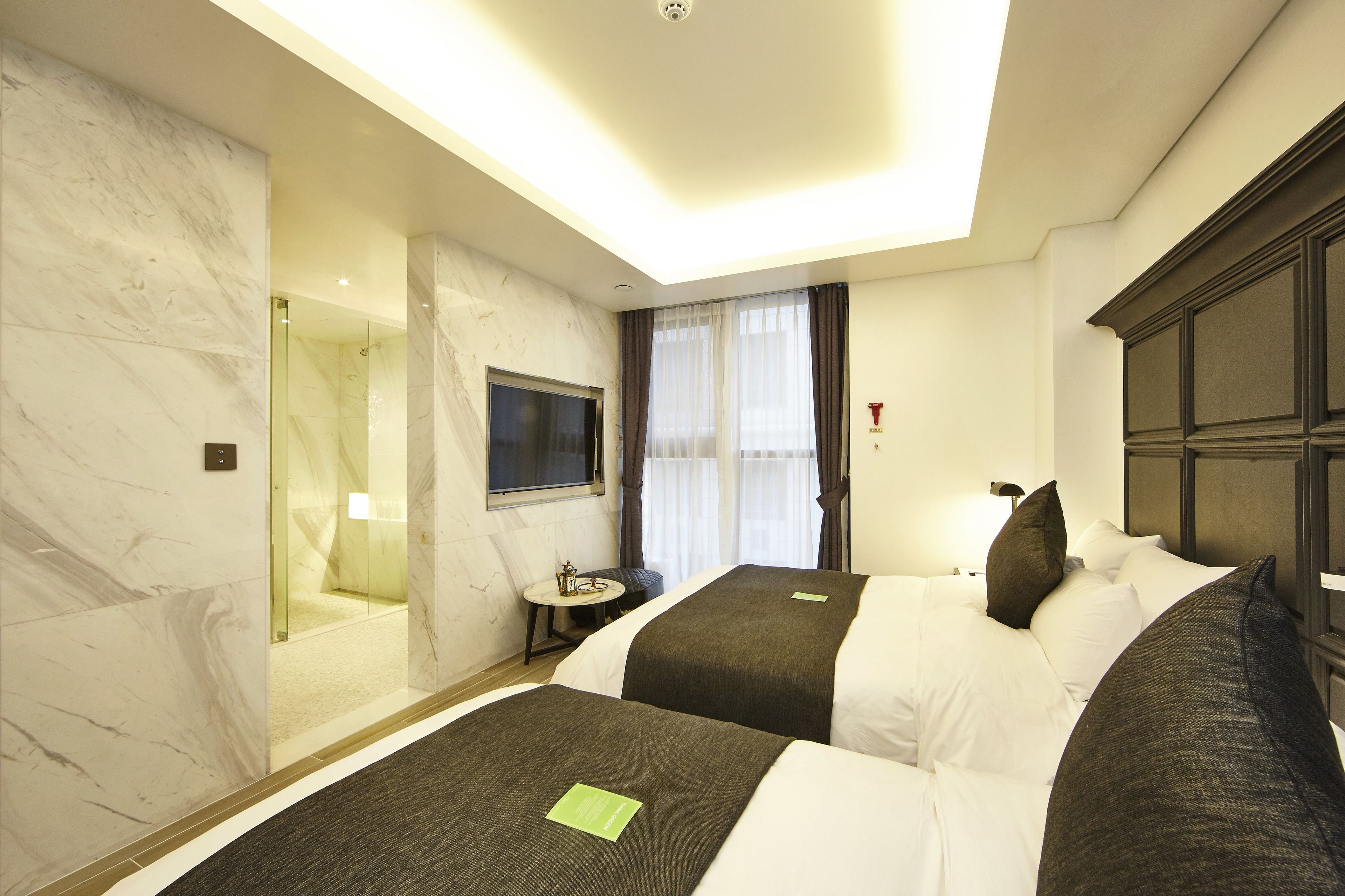 A hotel room with two beds, a TV, a small table, and a shower area.