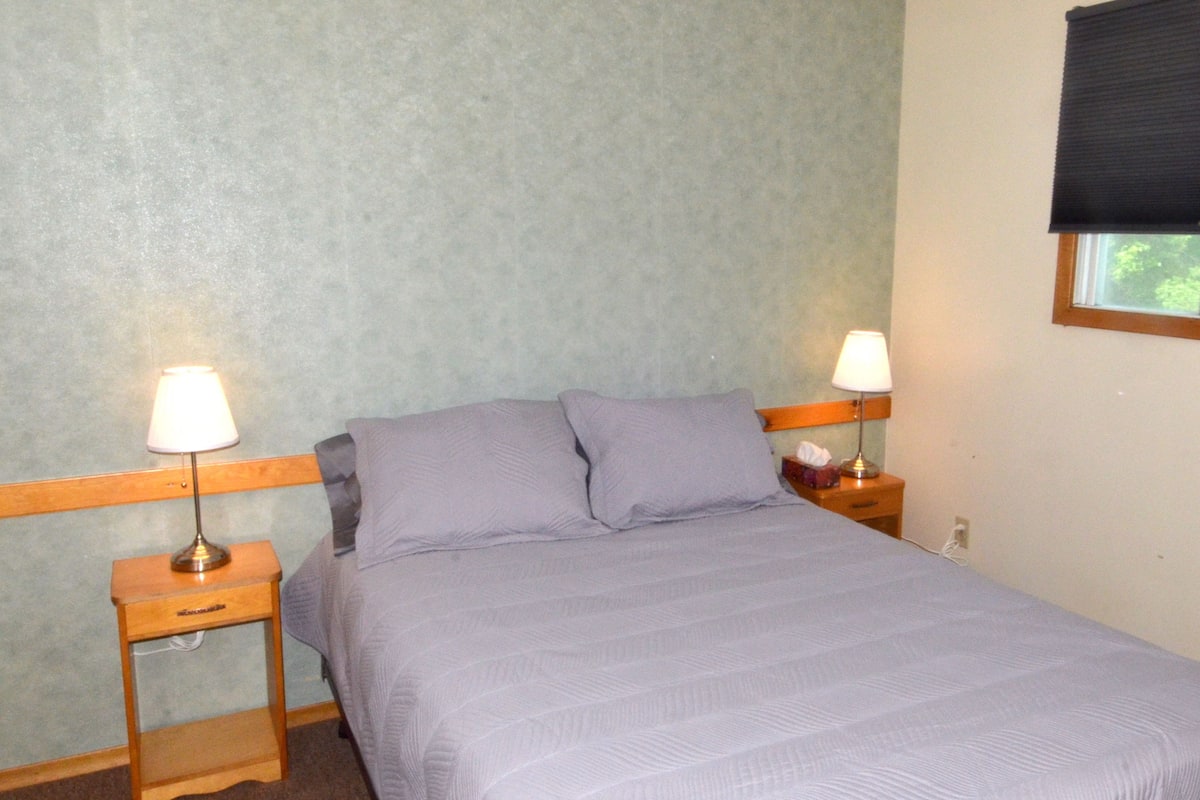 A small, neatly made bed with a light-colored bedspread in a room with a simple, functional design.