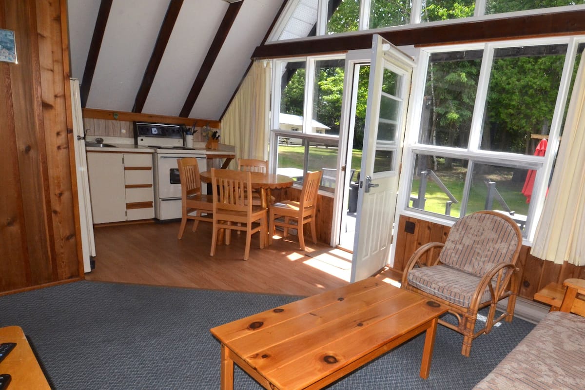 A cozy cabin interior with wooden furniture, a dining area, and large windows offering a view of the outdoors.