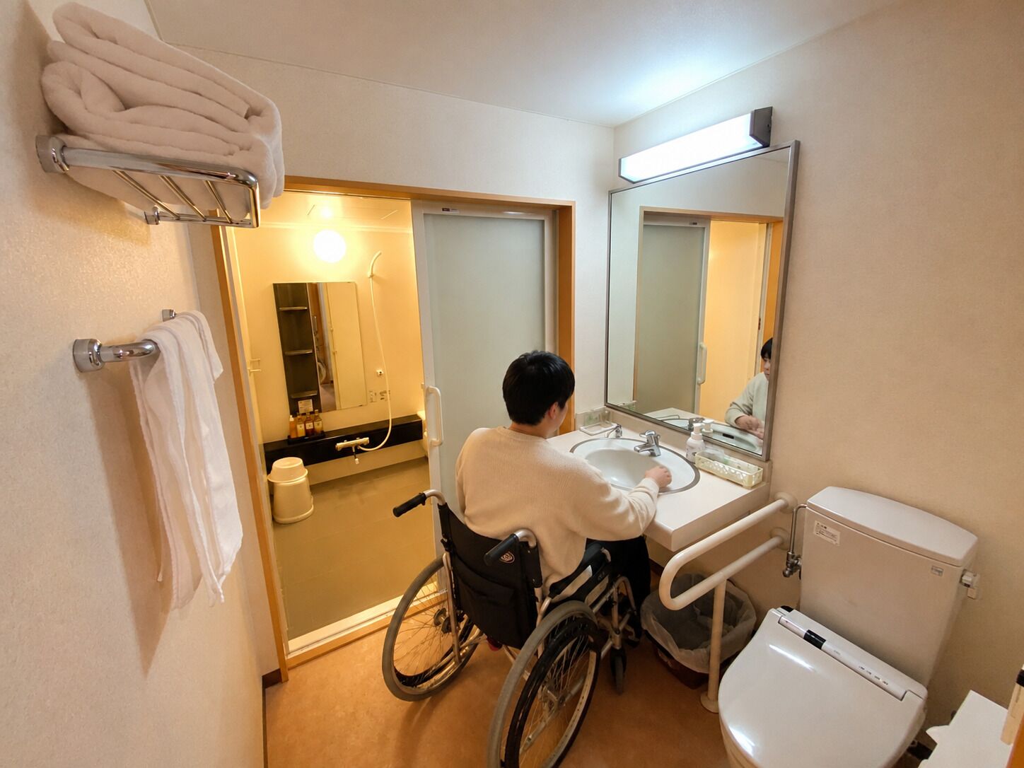 A wheelchair-accessible bathroom with a sink, toilet, and mirror.