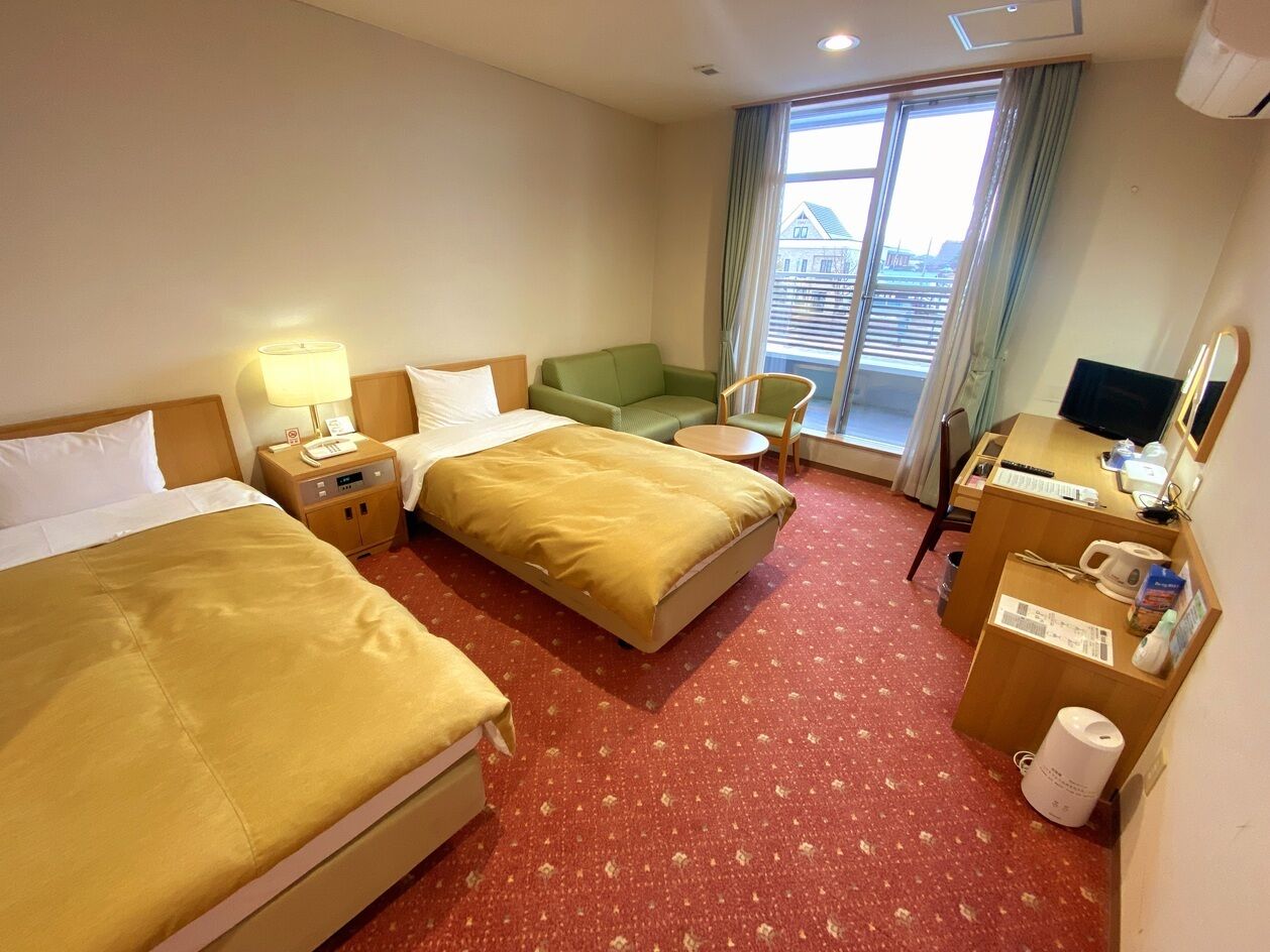 A hotel room with two beds, a desk, a chair, a TV, and a window with a view.
