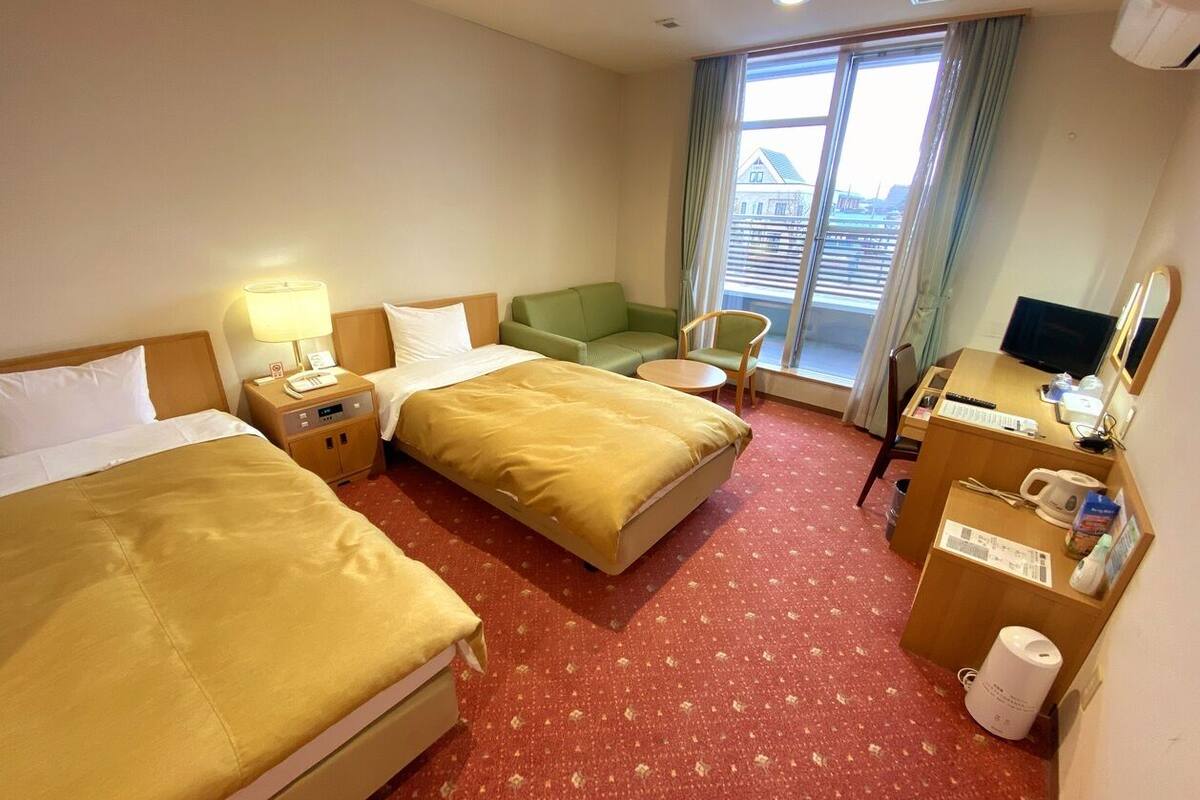 A hotel room with two beds, a desk, a chair, a TV, and a window with a view.