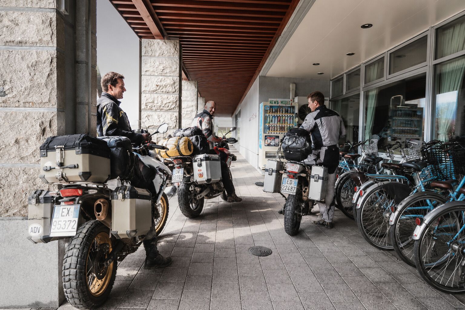 Un espace extérieur abrité où sont garées des motos et des vélos, avec des murs en pierre et un distributeur automatique.