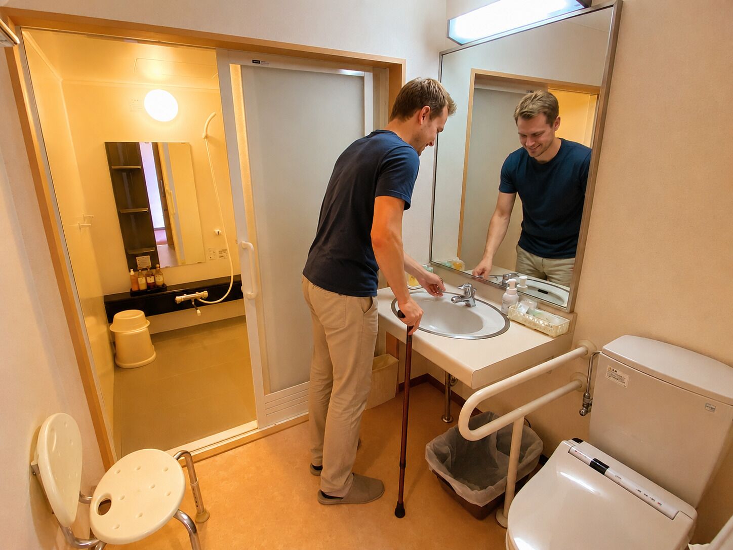 A bathroom with a sink, mirror, toilet, and a wheelchair-accessible toilet.