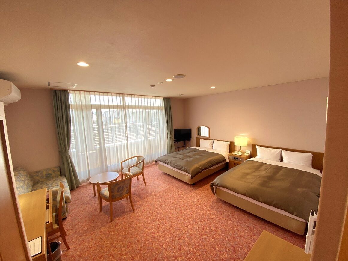 A hotel room with two beds, a sofa, a small table, and a TV.