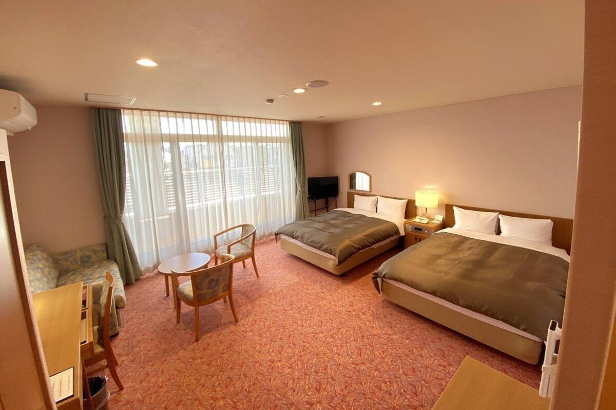 A hotel room with two beds, a sofa, a small table, and a TV.