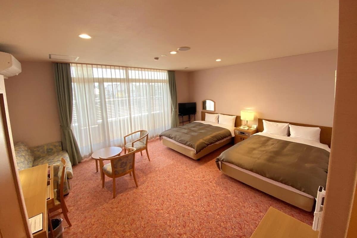 A hotel room with two beds, a sofa, a small table, and a TV.