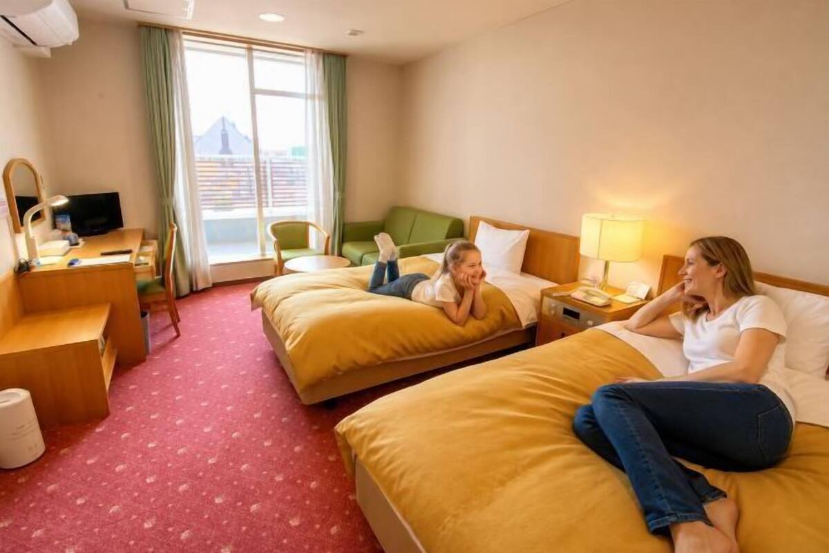 A hotel room with two beds, a desk with a computer, a chair, and a window with curtains.