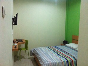 A small, single-bed room with a green accent wall, a desk with a chair, and a bedside table. - Living Peace House (Manado)