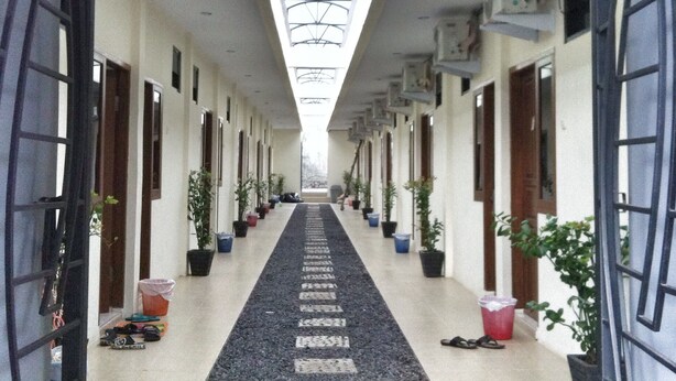 A corridor with a skylight ceiling, potted plants, and a patterned floor. - Living Peace House (Manado)