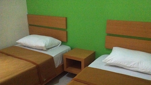 A room with two beds, each with a wooden headboard and white pillows. There is a small wooden nightstand between the beds. - Living Peace House (Manado)