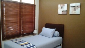 Una cama individual con un edredón a rayas, un cabecero y una ventana con persianas.