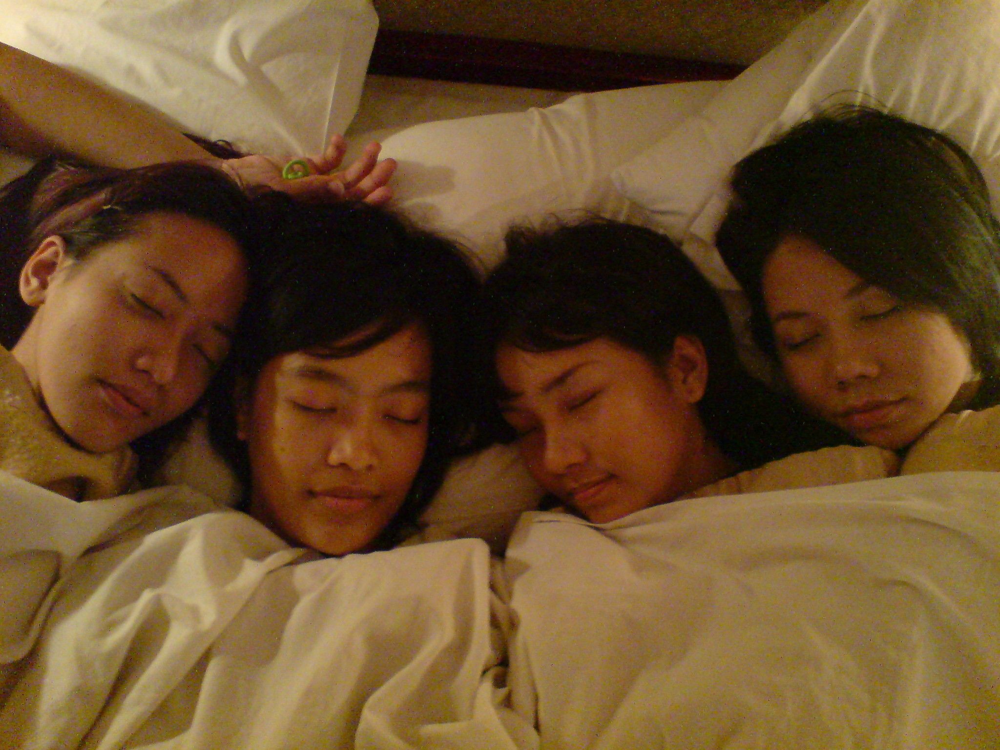 A group of people lying in bed with white bedding.