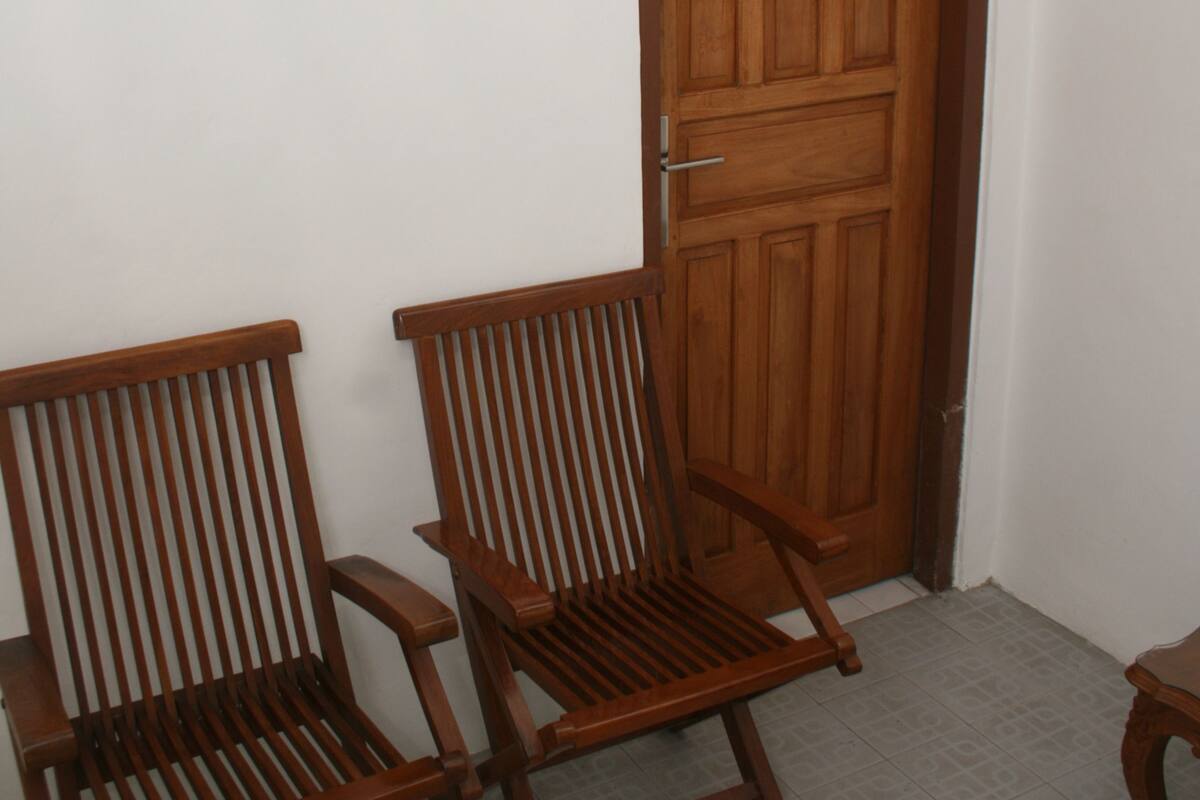 Quarto com duas cadeiras de madeira e uma porta de madeira com a letra 'M'.