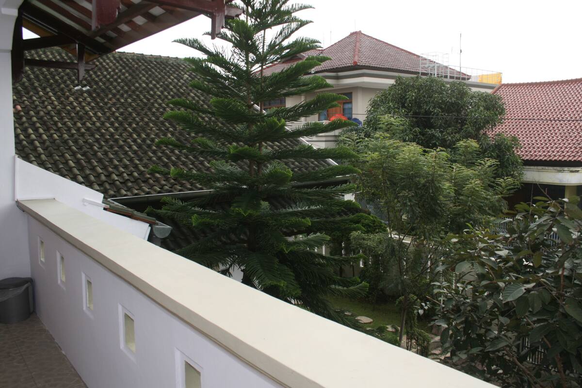 Um edifício com telhado de azulejos e varanda com vista para um jardim com várias árvores.