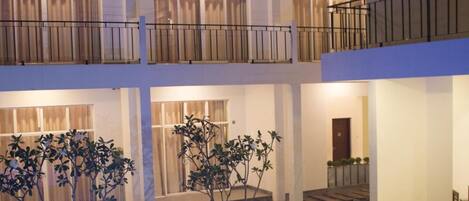 A multi-story hotel with a courtyard featuring a swimming pool, outdoor seating, and potted plants.