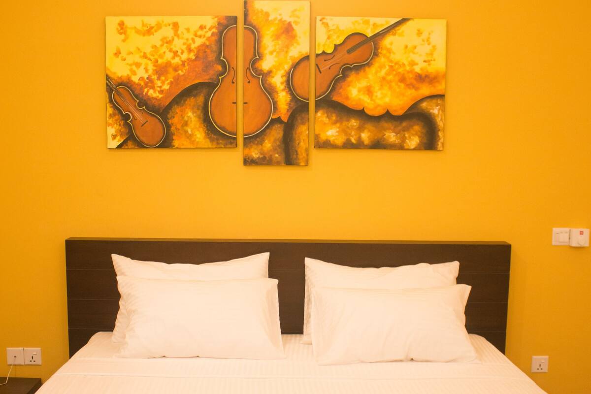 Habitación de hotel con cama, ropa de cama blanca y dos cuadros en la pared.