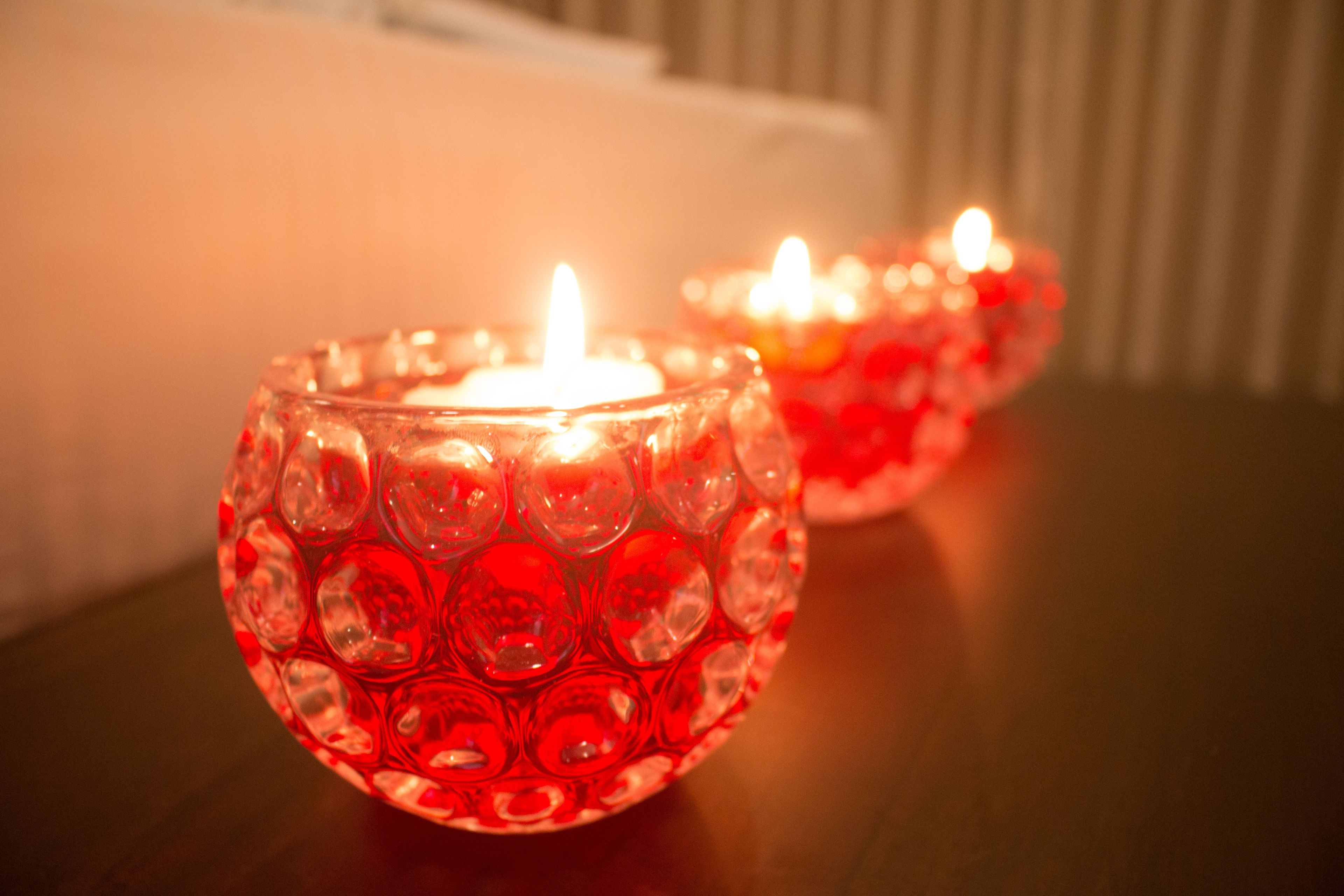 Two red glass candle holders with lit candles on a wooden surface.