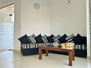A living room with a dark-colored sofa, a wooden coffee table, and a clock on the wall. - The Suite 262 (Negombo)