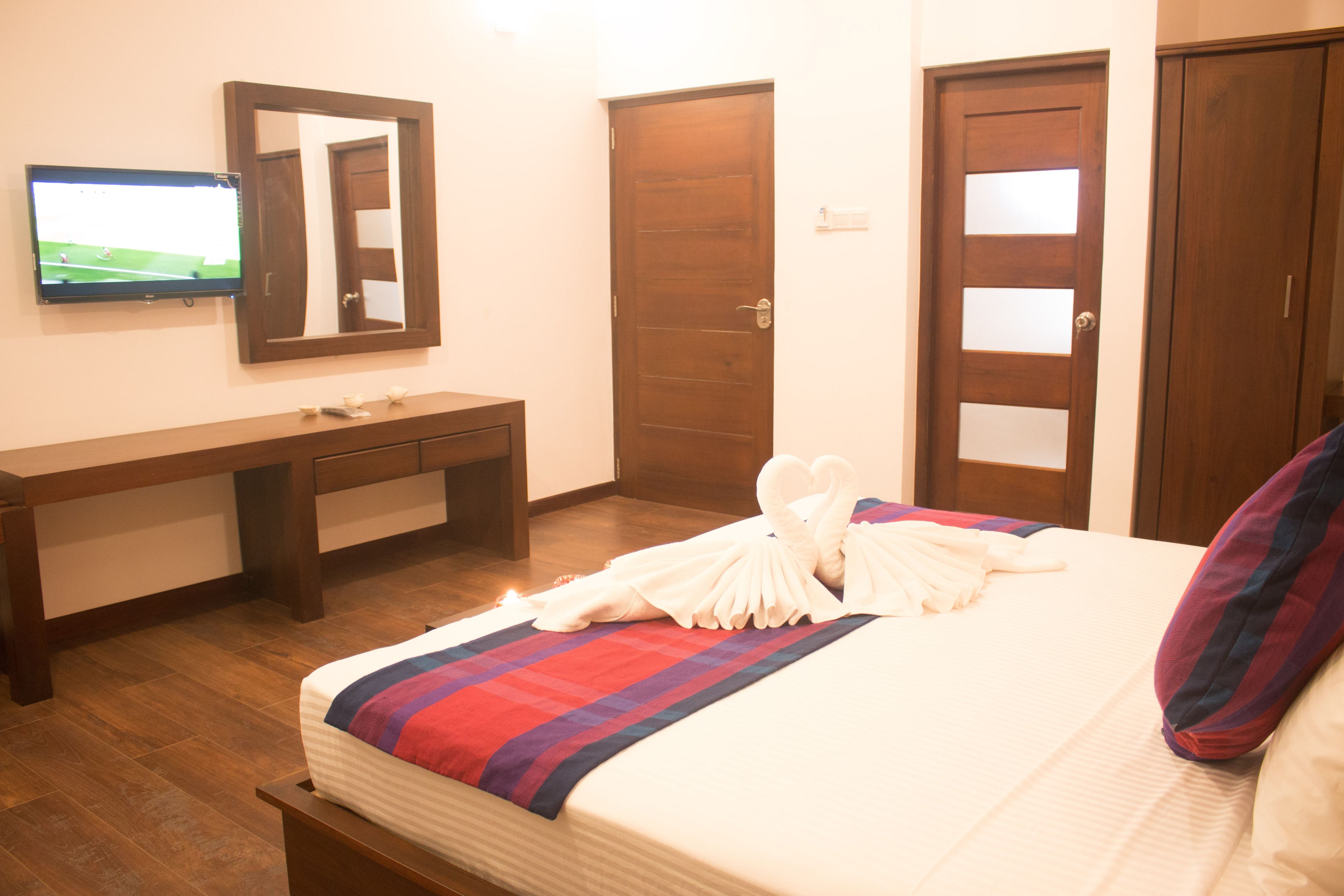 Habitación de hotel con cama, banco de madera, televisor y puerta.