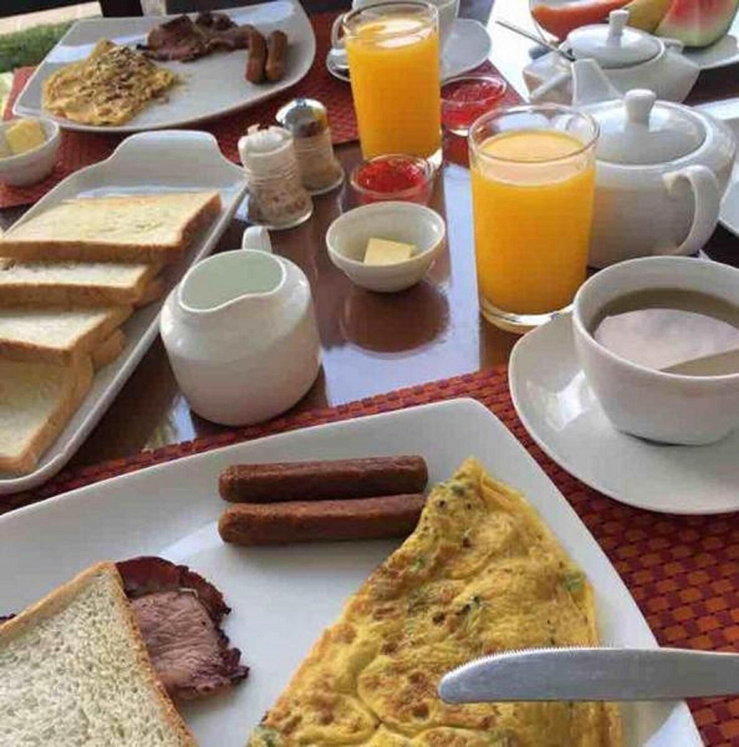 A breakfast table with various dishes including toast, sausages, a steak, an omelette, and orange juice.