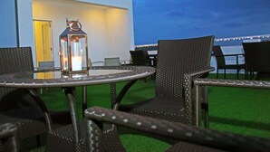 An outdoor seating area with wicker chairs and a table, a lantern, and a view of a building with a door and string lights. - The Suite 262 (Negombo)