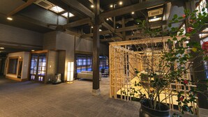 A spacious lobby with high ceilings, wooden beams, and a large potted plant. - Yufuin Baien Garden Resort (Yufu)