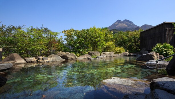 A clear pool with rocks, surrounded by trees and a wooden building. - Yufuin Baien Garden Resort (Yufu)